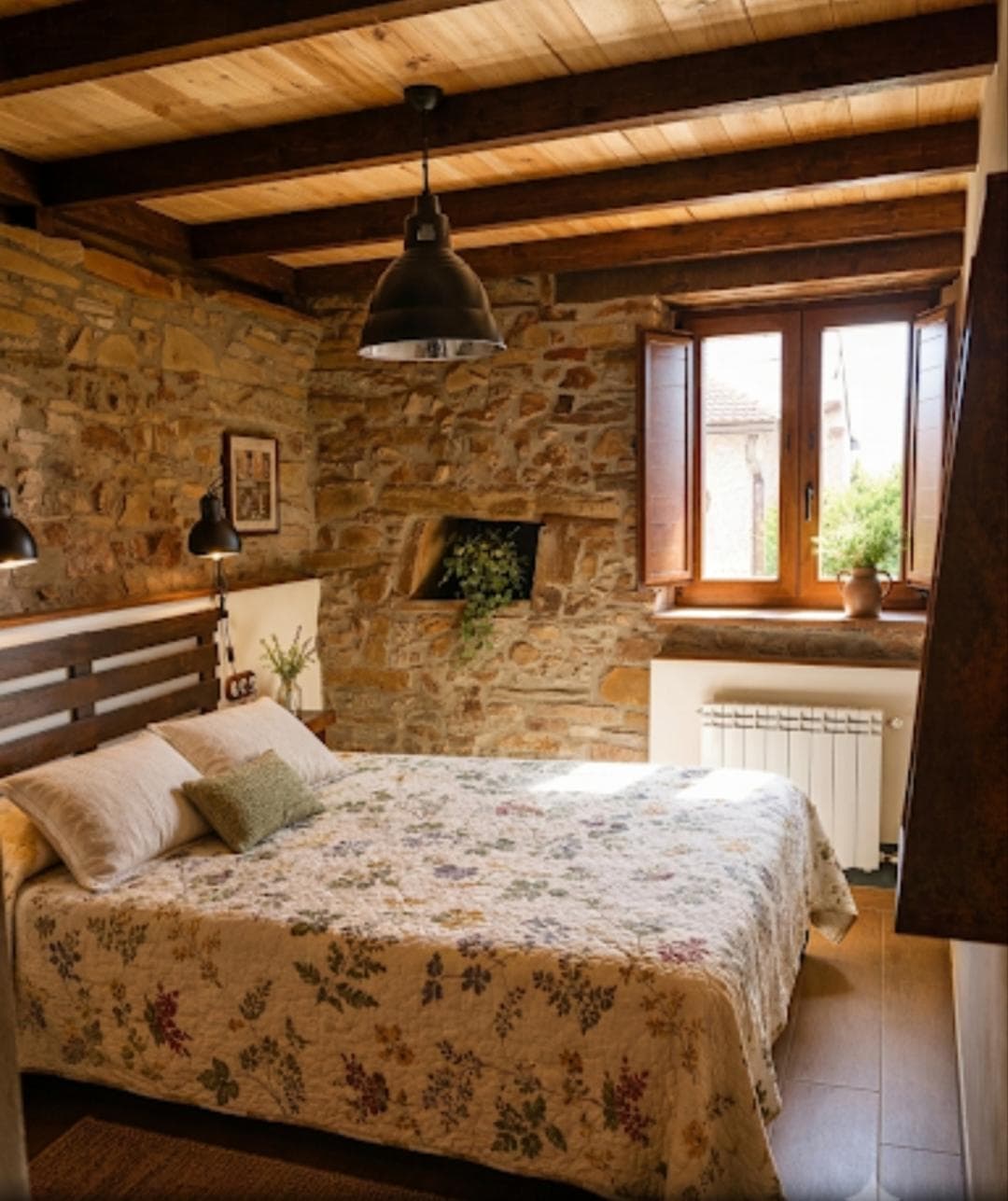 Suite Mostaza: cama de matrimonio con colcha floral, muro de piedra y techo de vigas